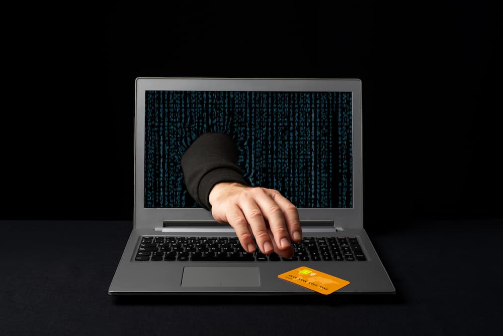 construction equipment identity theft hand reaching through laptop computer screen to grab a credit card