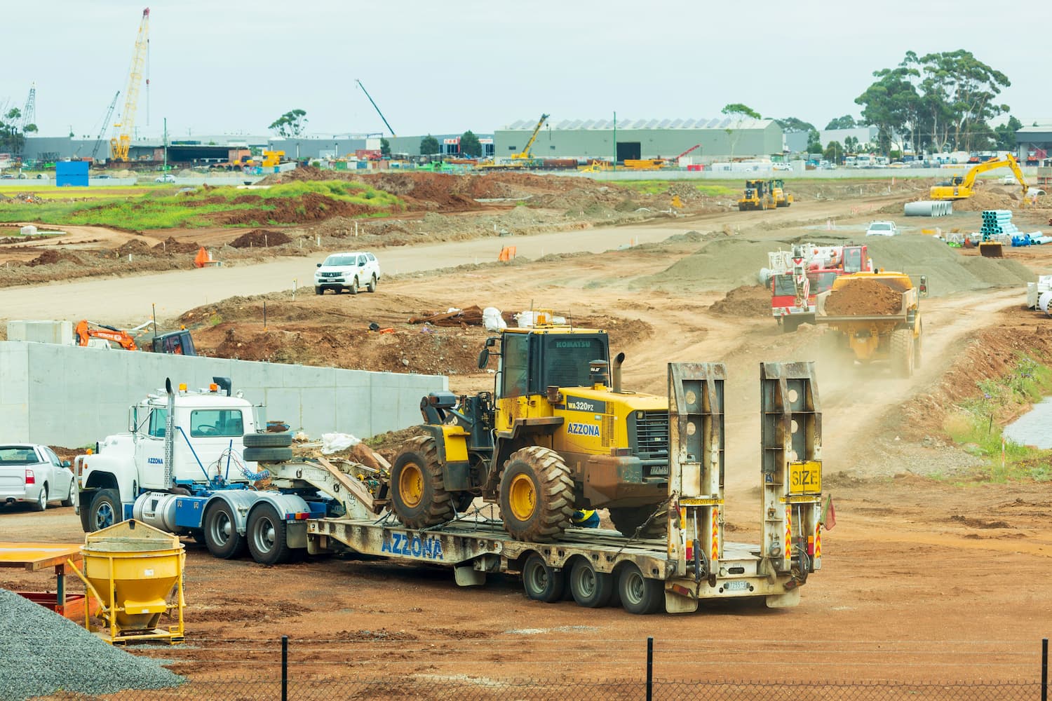 front heavy loader on equipment trailer pulled by truck on a construction site